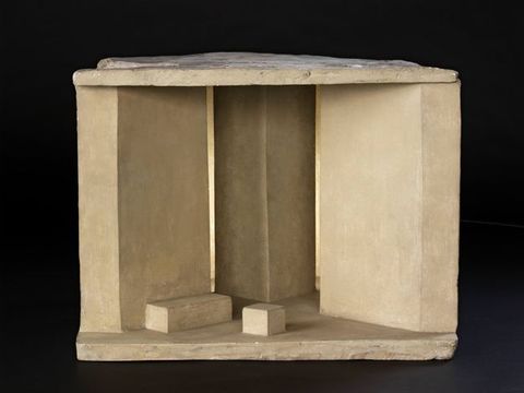 Model. The space of a stage is enclosed to each side by floor-to-curtain panels angled inwards. A square column is set at the back centre, so the footprint of the floor makes a W shape with a shallow peak.