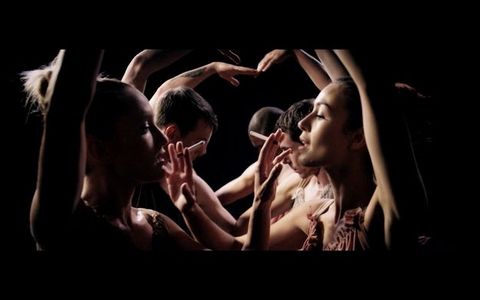 Pairs of dancers each hold up one arm to create an arch, as each lifts a cigarette to the other’s mouth with the other hand.