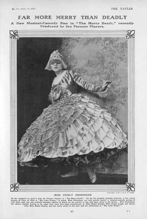 Page of a magazine. Black and white photograph of a woman in a costume with a domino mask, short veil, and a skirt with cascading ruffles. She stands posing against a background of a painted tree.